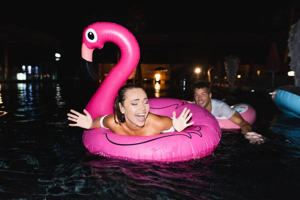 Focus selettivo della donna eccitata che nuota sul ring in piscina vicino al fidanzato di notte — Foto stock