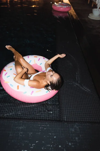 Selective focus of young woman lying on swim ring in pool at night — Stock Photo