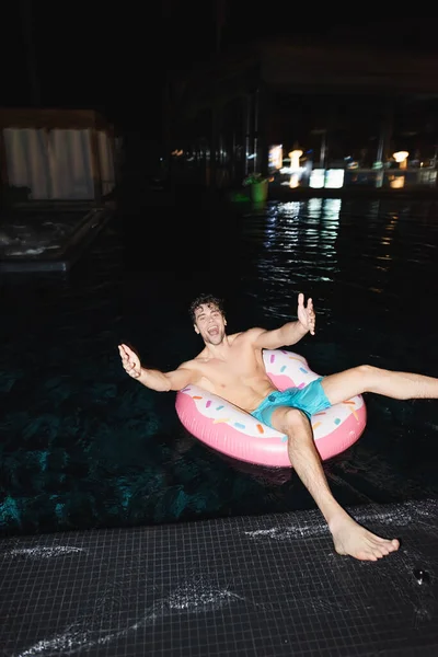 Вибірковий фокус збудженого м'язового чоловіка, який дивиться на камеру на плавальному кільці в басейні вночі — стокове фото