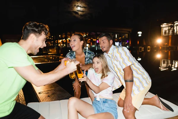 Вибіркове фокусування збуджених молодих людей, які вночі спілкуються з пивом біля басейну. — стокове фото