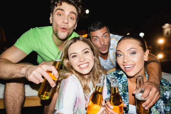 Focus selettivo di coppie che bucano bottiglie di birra durante la festa all'aperto di notte — Foto stock