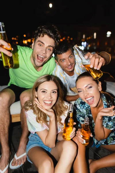 Focus selettivo di amici con bottiglie di birra che si divertono all'aperto di notte — Foto stock