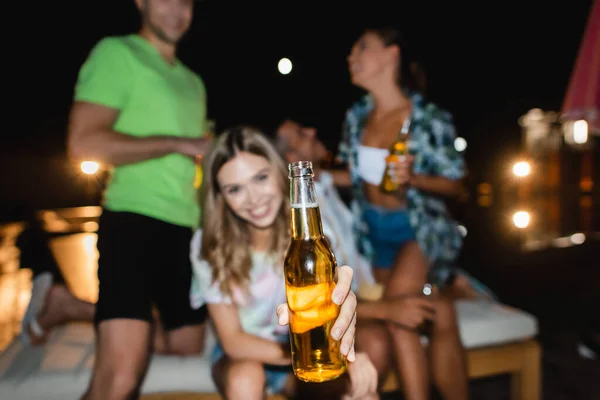 Вибіркове фокусування жінки на тому, щоб показати пляшку пива близьким хлопцям і друзям на вулиці вночі. — стокове фото