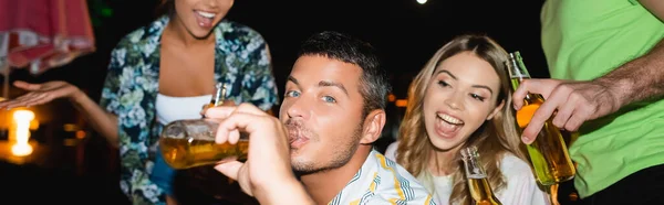 Website header of man drinking beer near excited friends outdoors at night — Stock Photo