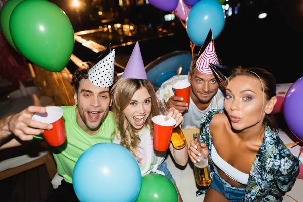 Freunde halten bei Party nachts Einwegbecher und Bierflaschen in der Nähe von Luftballons — Stockfoto