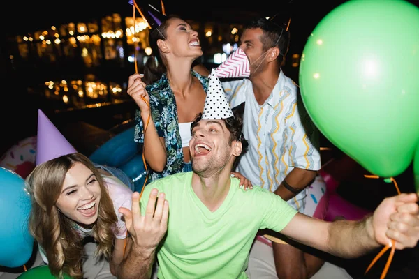 Selective focus of friends having fun during party with balloons outdoors at night — Stock Photo