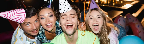 En-tête de site Web d'amis excités dans les casquettes de fête regardant la caméra près de la piscine la nuit — Photo de stock