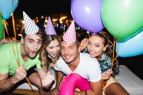 Молоді друзі дивляться на камеру під час вечірки з повітряними кулями вночі — стокове фото