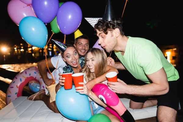 Selective focus of women clinking with disposable cups near balloons during party near swimming pool at night — Stock Photo