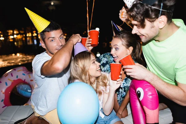 Selektiver Fokus von Freunden beim Anstoßen mit Einwegbechern in der Nähe von Luftballons während einer Party in der Nacht — Stockfoto