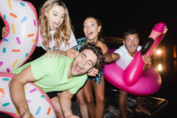 Selective focus of excited friends with swim rings standing near pool at night — Stock Photo