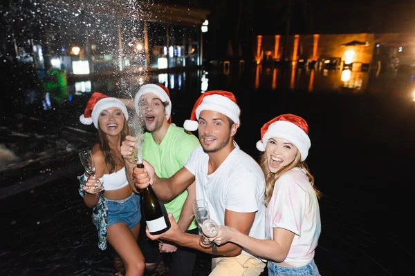 Selective focus of friends opening bottle of champagne while celebrating new year at night outdoors — Stock Photo