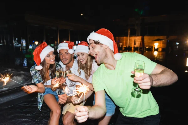 Focus selettivo di amici con scintille clinking con champagne vicino alla piscina di notte — Foto stock