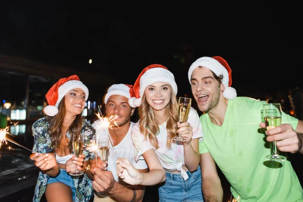 Jeunes amis célébrant le Nouvel An avec du champagne et des étincelles en plein air la nuit — Photo de stock