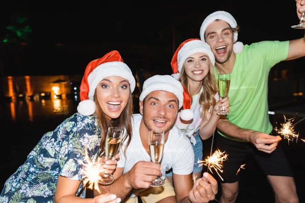 Selective focus of young people celebrating new year with champagne and sparklers at night outdoors — Stock Photo