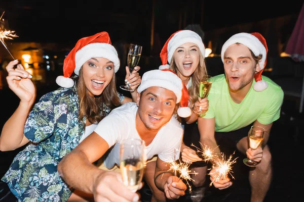 Selektiver Fokus aufgeregter Freunde, die Wunderkerzen und Sektgläser in der Hand halten, während sie in der Nacht Neujahr feiern — Stockfoto