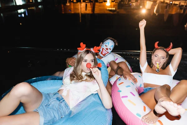 Вибірковий фокус молодих друзів з лоскотами на плавальних кільцях в басейні вночі — стокове фото