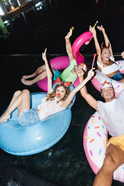 Freunde blicken bei Party auf Schwimmringe im Pool in die Kamera — Stockfoto