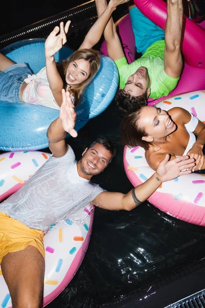 Vista de ángulo alto de amigos divirtiéndose en la piscina durante la fiesta por la noche - foto de stock