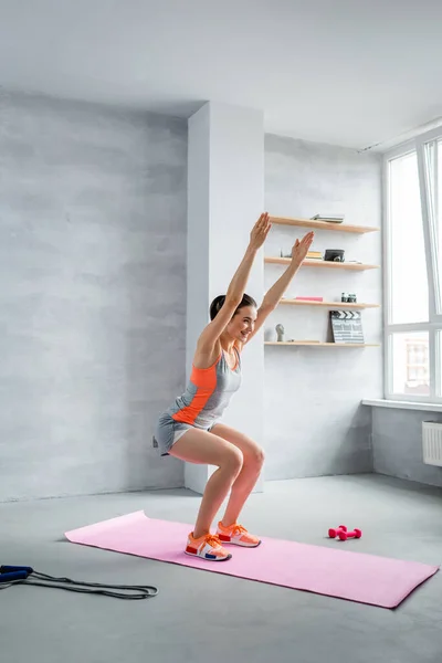 Side view of sportswoman squatting with hands in air near sport equipment — Stock Photo