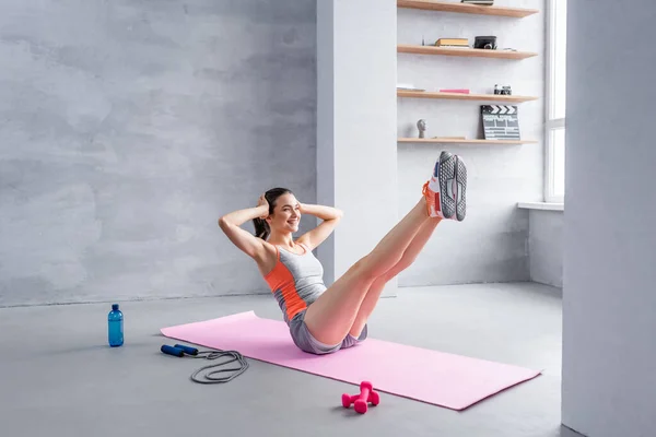 Sportlerin mit ausgestreckten Beinen macht Bauch auf Fitnessmatte in der Nähe von Sportgeräten — Stockfoto