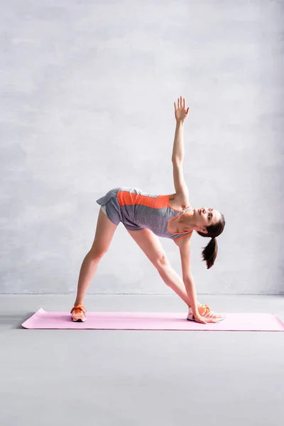 Sportswoman avec les mains tendues échauffement sur tapis de fitness sur fond gris — Photo de stock