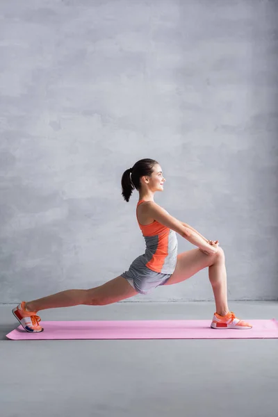 Seitenansicht der Sportlerin beim Ausfallschritt auf Fitnessmatte auf grauem Hintergrund — Stockfoto