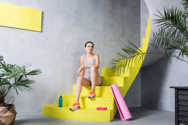 Deportiva mirando hacia otro lado y sentada en escaleras cerca de equipos deportivos - foto de stock