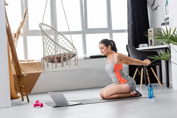 Спортсменка греется возле ноутбука во время онлайн-тренировок дома — стоковое фото