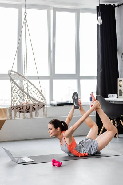 Женщина тренируется рядом с ноутбуком и гантелями на фитнес-коврике в гостиной — стоковое фото