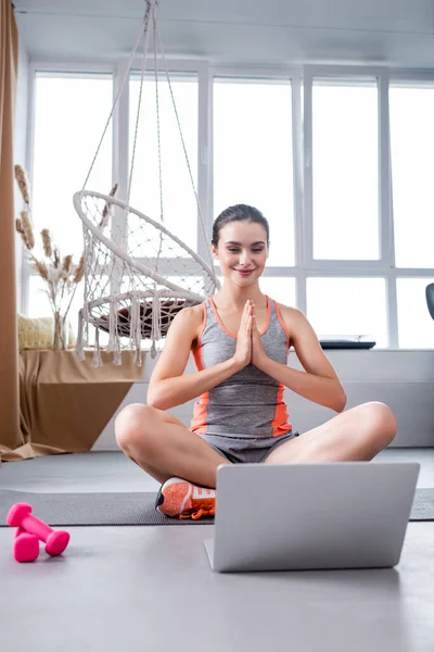 Enfoque selectivo de la deportista sentada en la colchoneta de fitness cerca de pesas y portátil en casa - foto de stock