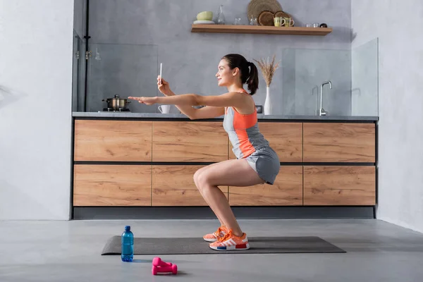 Боковой вид женщины, использующей смартфон во время тренировки на фитнес-коврике дома — стоковое фото