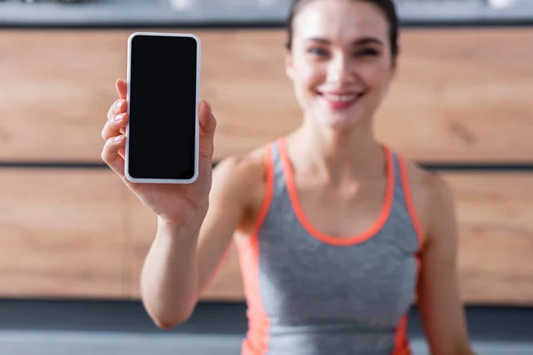 Enfoque selectivo de la deportista mostrando teléfono inteligente con pantalla en blanco en casa - foto de stock