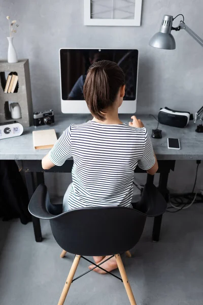 Vista trasera del freelancer sentado cerca de la computadora, smartphone y reservar en la mesa en casa - foto de stock