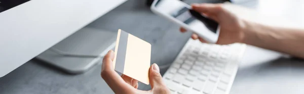 Fotografía panorámica del freelancer con tarjeta de crédito y smartphone cerca del ordenador - foto de stock