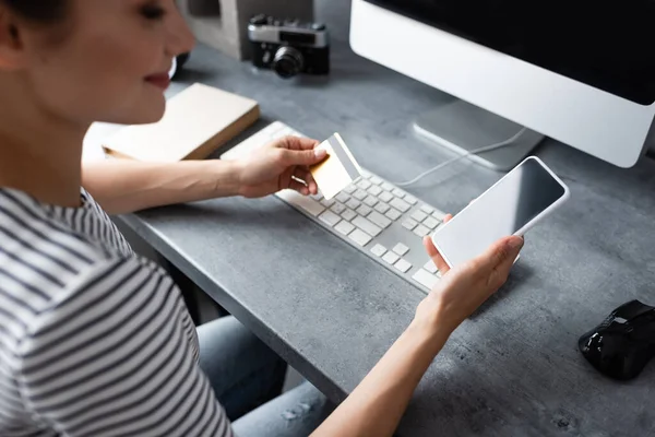 Selective focus of young freelancer using smartphone and credit card while working at home — Stock Photo