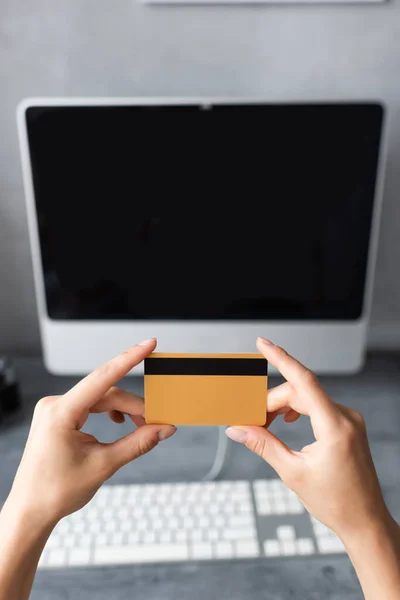 Обрезанный вид женщины, держащей кредитную карту рядом с компьютером дома — стоковое фото