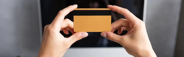 Imagem horizontal da mulher segurando cartão de crédito perto do monitor do computador em casa — Fotografia de Stock