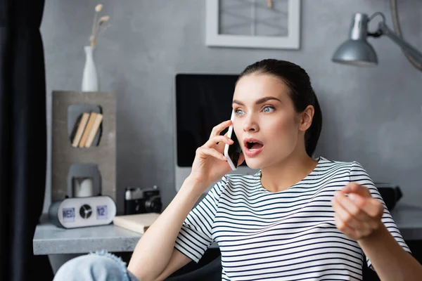Selective focus of shocked freelancer talking on smartphone at home — Stock Photo
