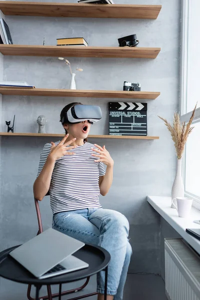 Selective focus of shocked woman in vr headset sitting near laptop on coffee table in living room — Stock Photo