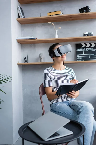 Enfoque selectivo del teletrabajador usando auriculares vr mientras escribe en un portátil cerca de la computadora portátil en la mesa de café - foto de stock