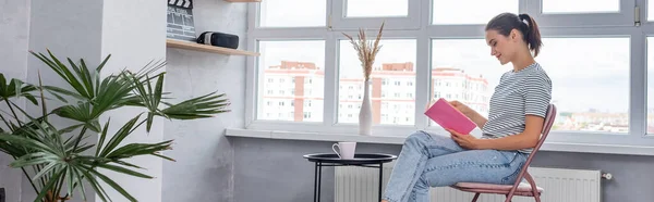 Website header of young woman reading book near cup on coffee table at home — Stock Photo