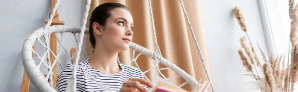 Website header of young woman with book looking away in hanging armchair — Stock Photo