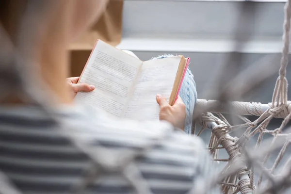 Foco seletivo da mulher ler livro na poltrona pendurada — Fotografia de Stock
