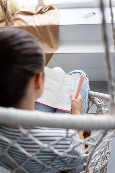 Задний вид молодой женщины, читающей книгу, сидя в висящем кресле — стоковое фото