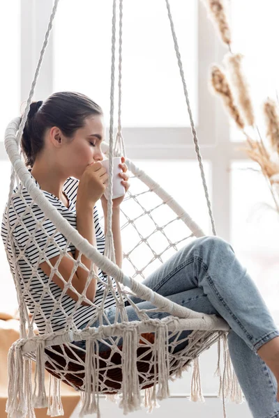 Concentration sélective de la femme buvant du thé tout en étant assis dans un fauteuil suspendu — Photo de stock