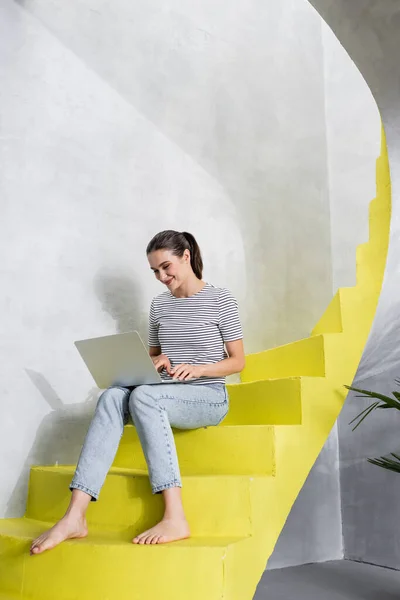 Barefoot freelancer using laptop on stairs at home — Stock Photo