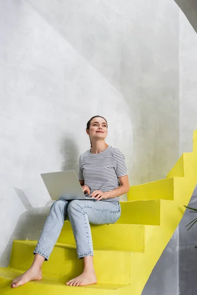 Brunette woman using laptop while sitting on stairs at home — Stock Photo