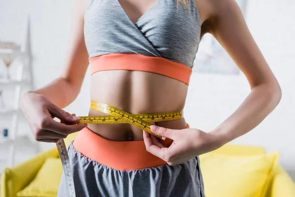 Vue recadrée d'une sportive mesurant sa taille fine avec du ruban adhésif à la maison — Photo de stock