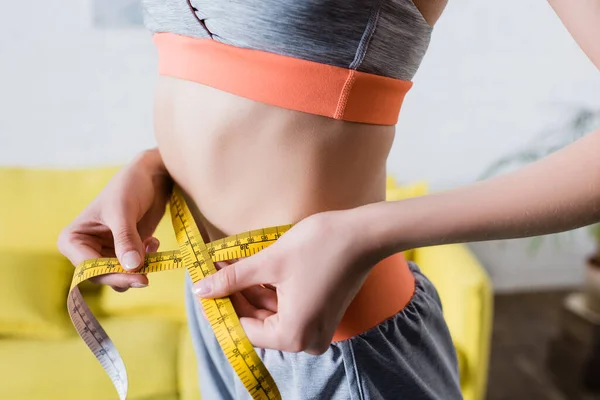 Cropped view of sportswoman measuring thin waist with tape at home — Stock Photo